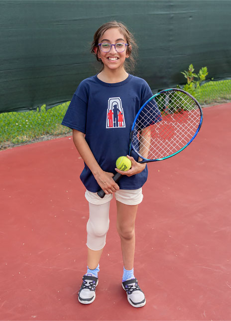 A young female leg amputee holds a tennis racket and ball while standing on a tennis court.