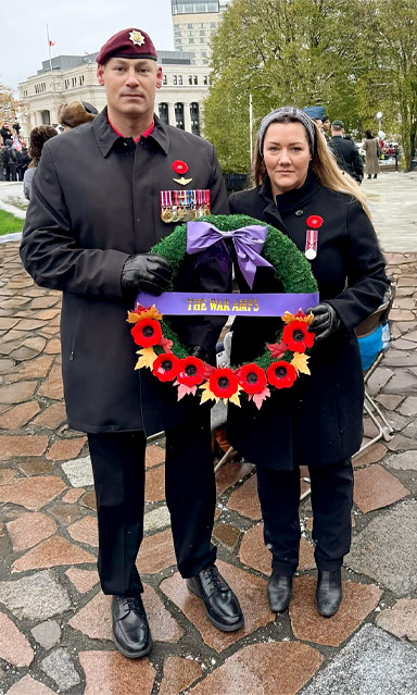 An adult male double leg amputee and his wife hold a War Amps wreath.