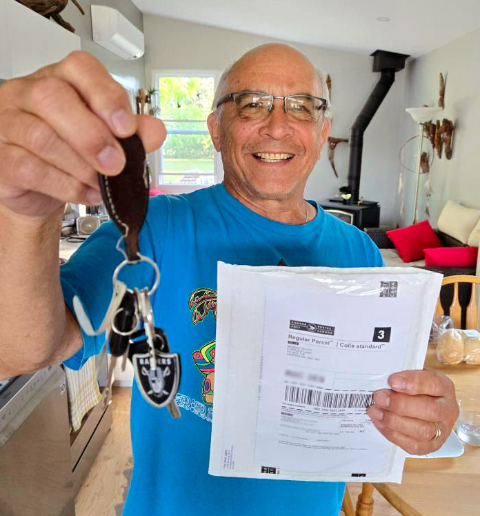 An older man holds up a set of keys and a courier envelope.