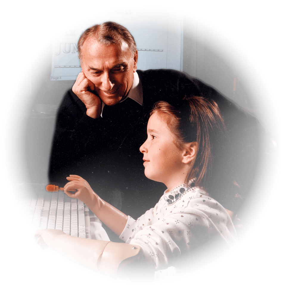 Cliff Chadderton sitting with a young double arm amputee in front of a computer monitor.