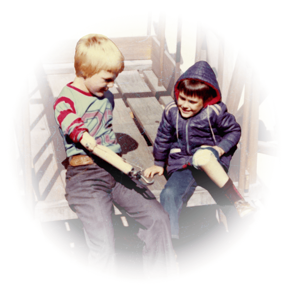A young male arm amputee sits beside a young male leg amputee on a wooden horse cart at the farm. 