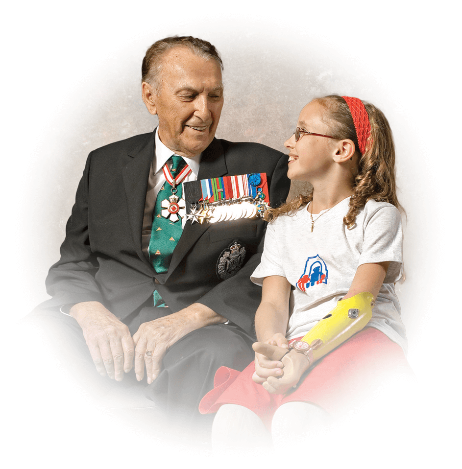 Cliff Chadderton wears his service medals and is seated next to a young girl who is an arm amputee.