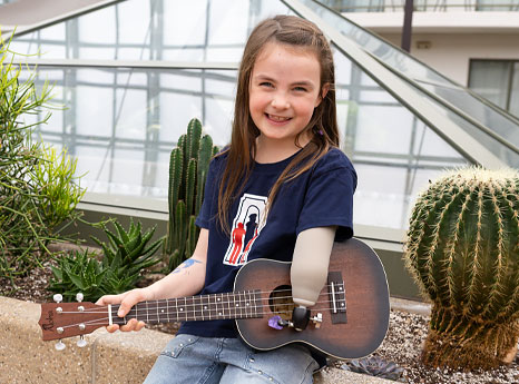 A young female amputee uses a device attached to her artificial arm to play a ukulele.